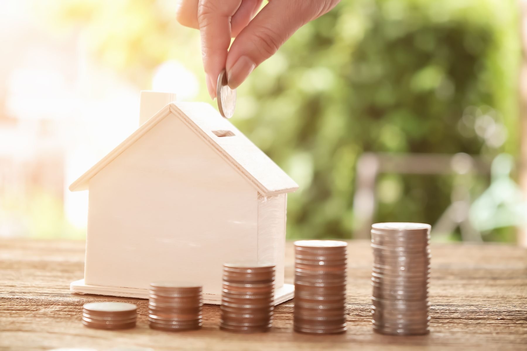 Piggy bank in shaped of house and a hand is putting a coin into it.
