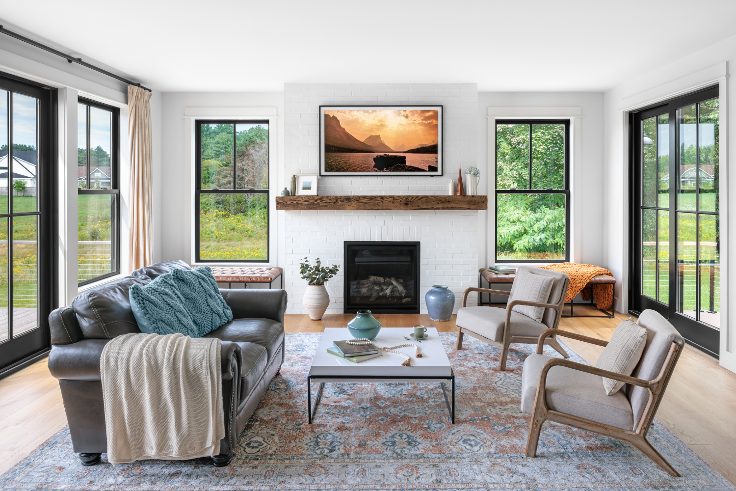 A brightly lit living room with black casement windows on the far end and sliding patio doors on either side. There is furniture arranged in the middle of the room.