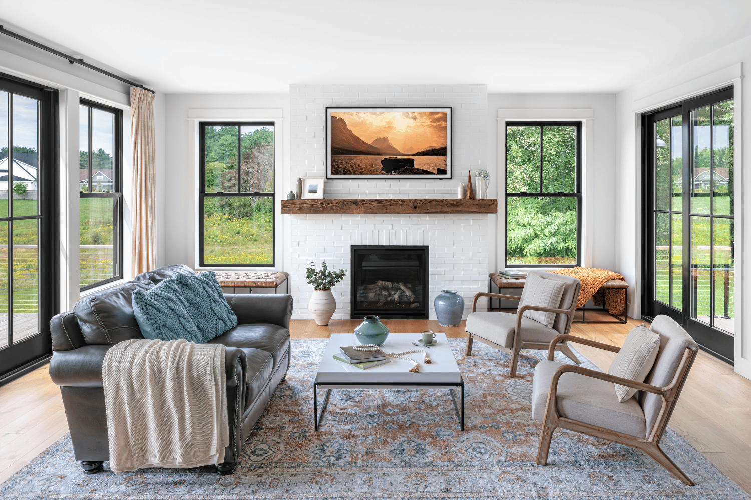 A brightly lit living room with black casement windows on the far end and sliding patio doors on either side. There is furniture arranged in the middle of the room.