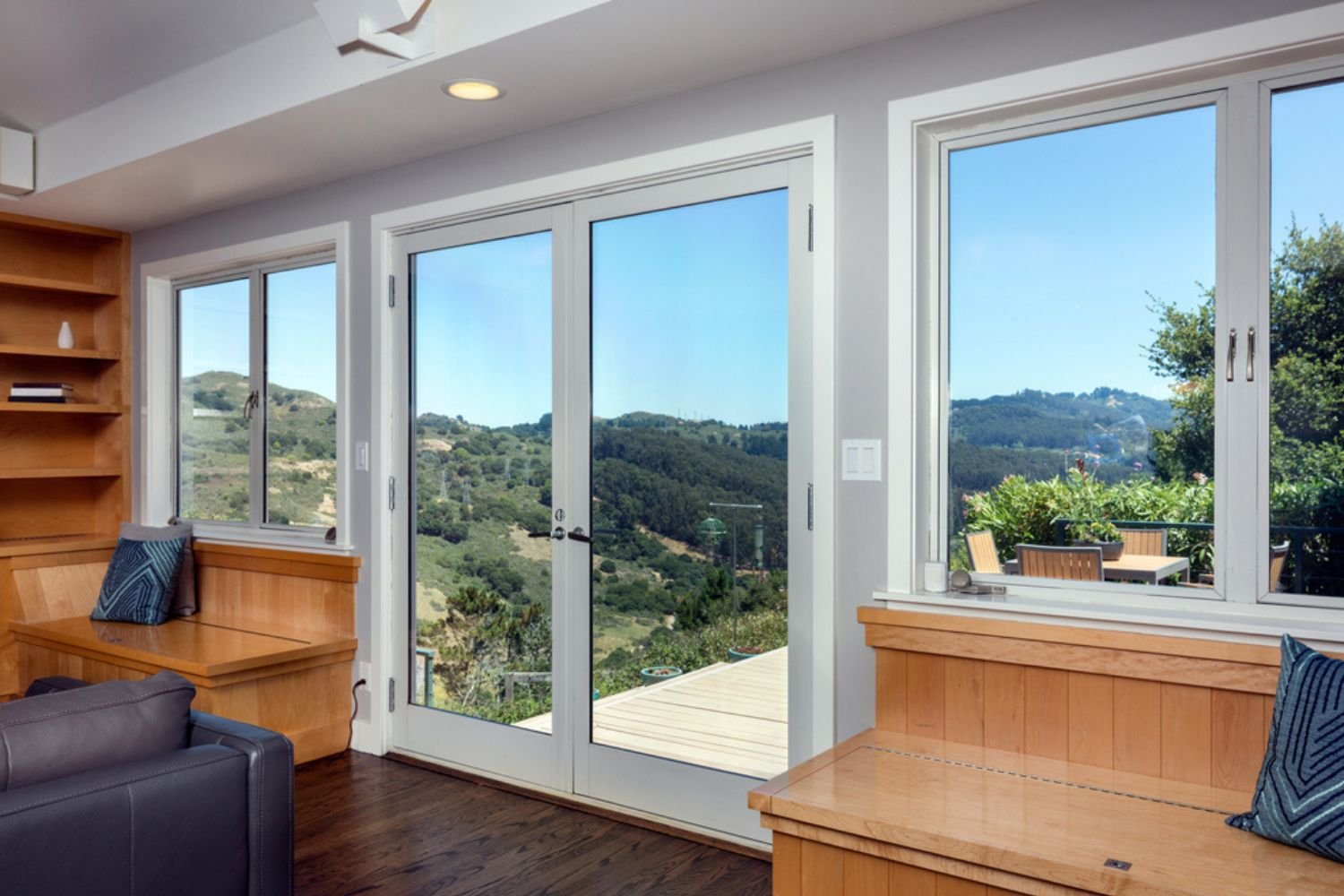 Living room with a patio door and casement windows that look out on to wood hills.
