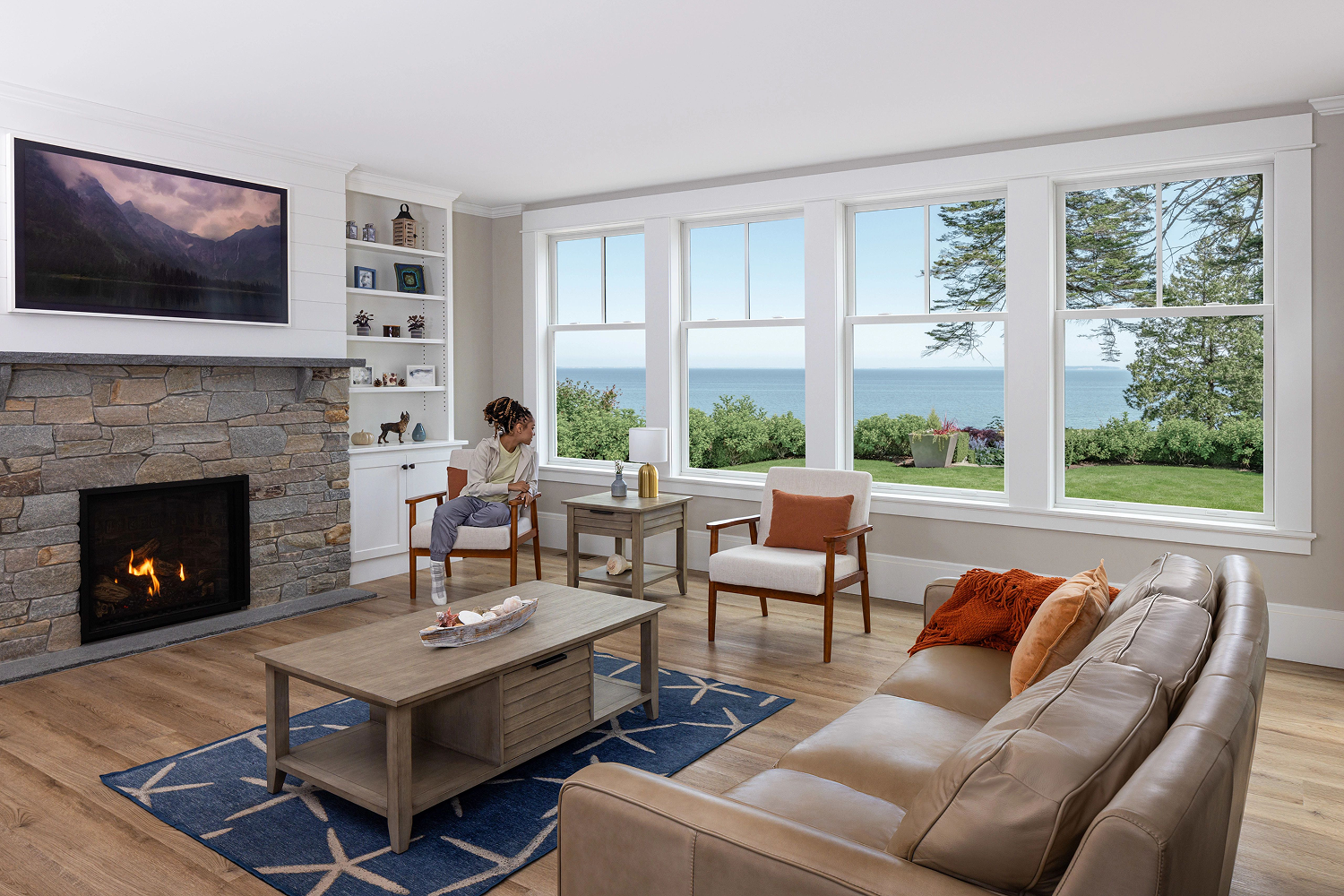 White living room with a wood floor featuring one side of the room lined in white double hung windows that let in lots of natural light. 