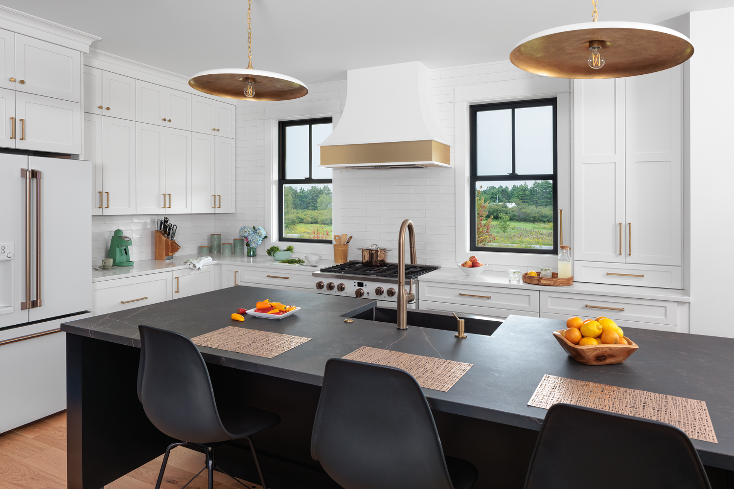 Two double hung windows on each side of the stove in a white kitchen with a black counter island in the middle.