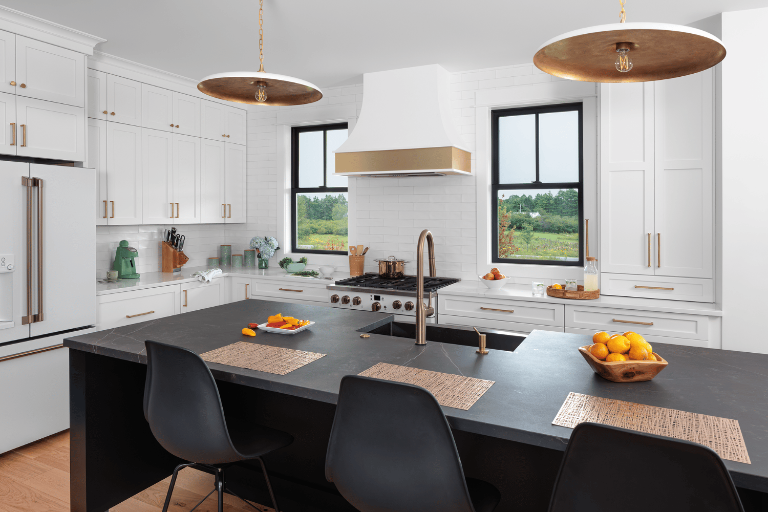 Two double hung windows on each side of the stove in a white kitchen with a black counter island in the middle.