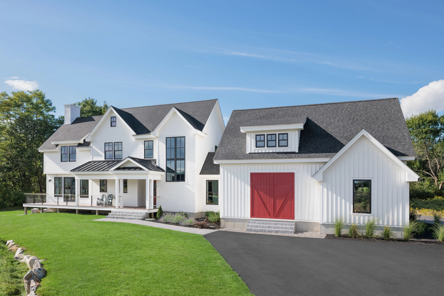 A charming white farmhouse featuring a red door, a driveway, and beautiful composite windows from  Renewal by Andersen