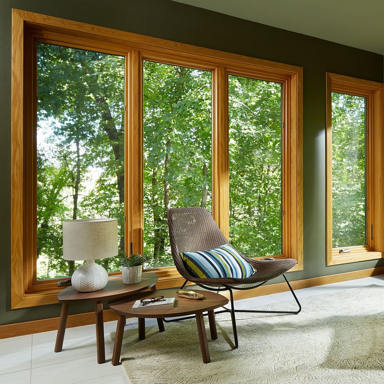 A living room in a shaded area with lots of trees outside. The windows are wood interior, with no grilles. Floor to ceiling casements.